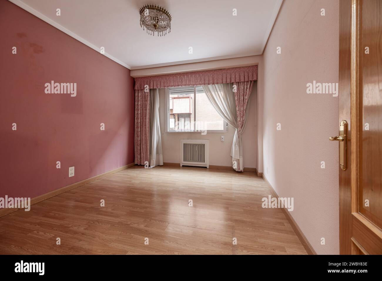 Living room with terracotta and pale pink walls, oak carpentry on doors and floors, curtains and curtains with matching skirts on the wall with window Stock Photo