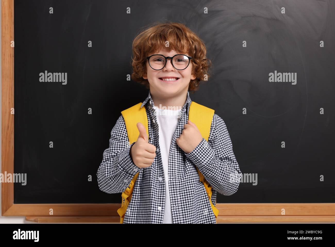 Happy schoolboy in glasses with backpack showing thumb up gesture near ...
