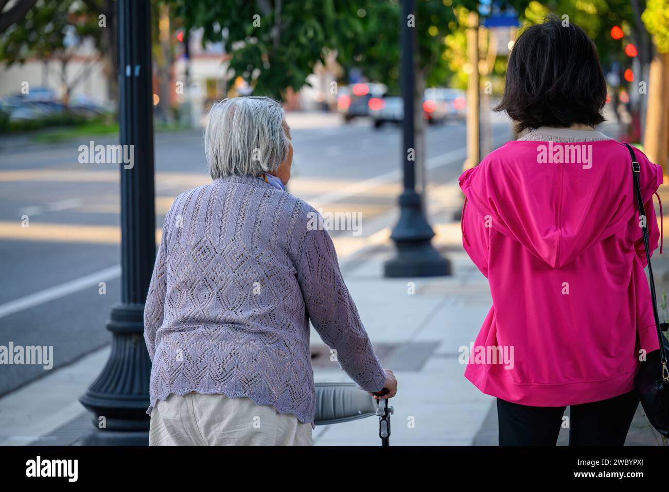 Senior woman walking using a mobility walker on the pedestrian footpath, accompanied by her daughter. Stock Photo