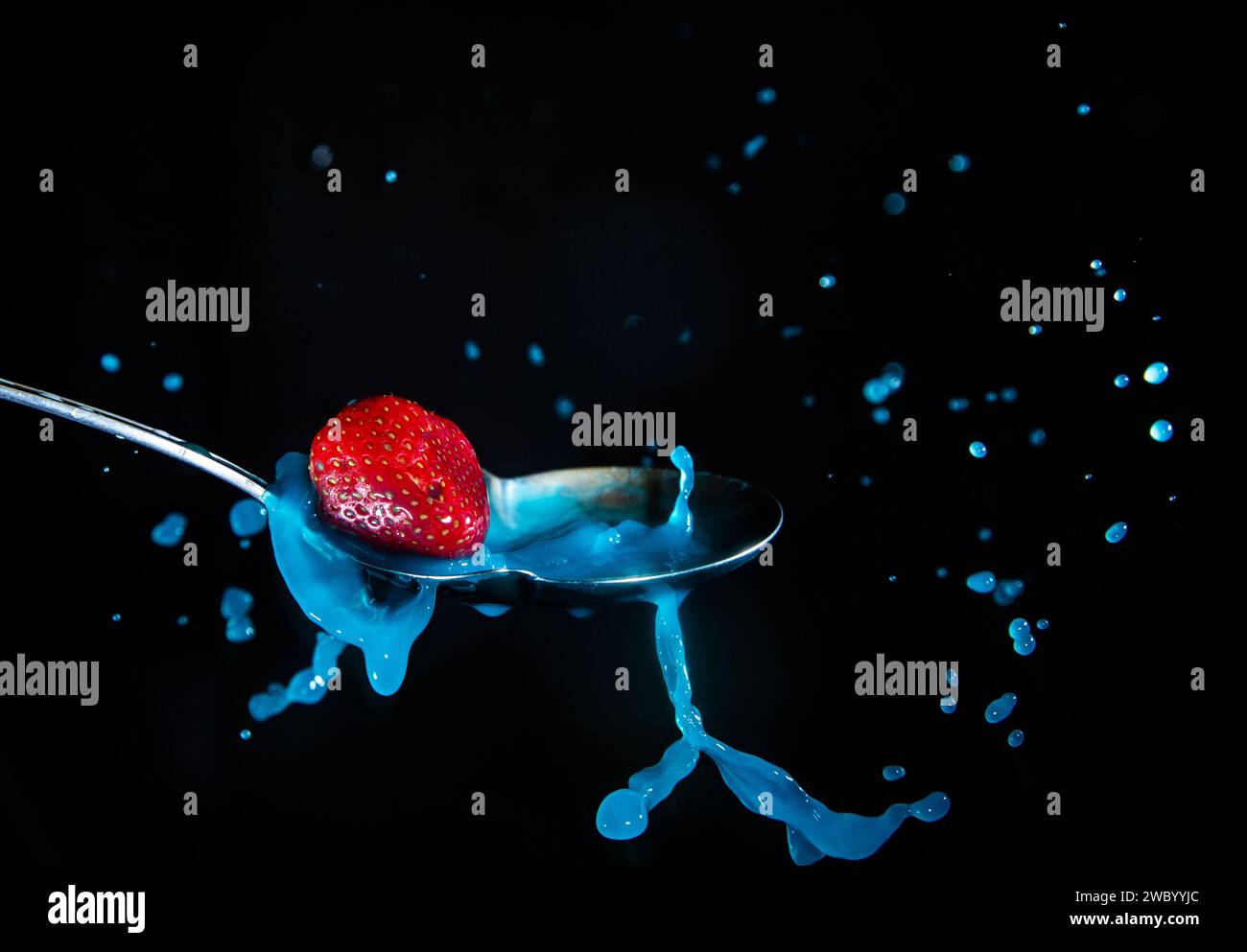 Strawberry splashing into a milky blue liquid in a spoon Stock Photo