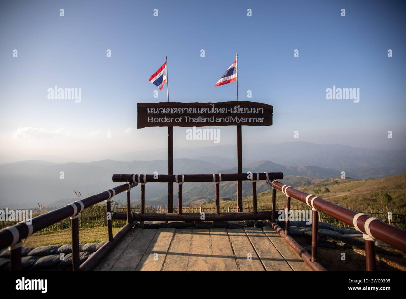 A sign depicting the Thai-Myanmar border with Thailand flags on top. The Chang Moob Military Outpost now turned into a tourist attraction spot, used to be a Thai Royal Army location to prevent drug smuggling and keep an eye on other suspicious activities on the Myanmar side (mostly in the 1990s). Also called the 'Doi Tung Trenches' It starts off with a narrow pathway through high bamboo fences before reaching the main spot with deep trenches along the northernmost sections of the Thai-Myanmar border, with a stunning view of Myanmar mountains. Stock Photo