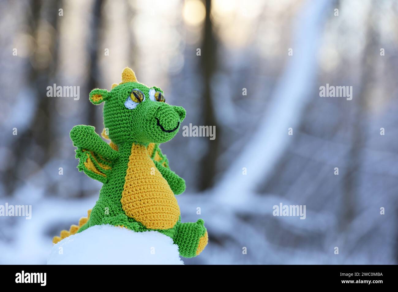 Knitted dragon in a snow on winter forest background, greeting card. Symbol of Chinese New Year 2024 Stock Photo