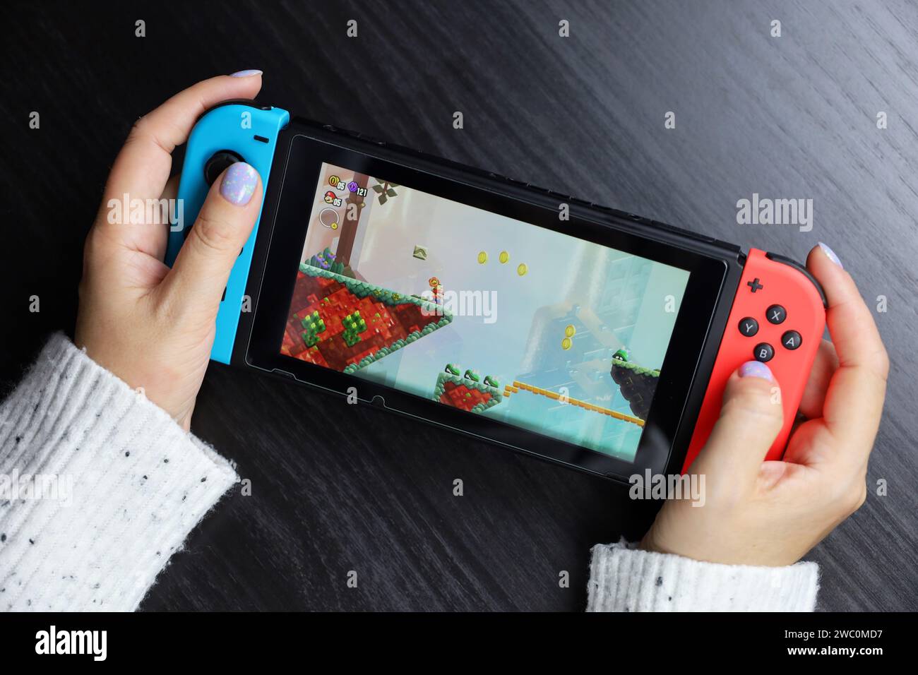 Girl playing Super Mario Bros. Wonder game on Nintendo Switch console in handheld mode Stock Photo