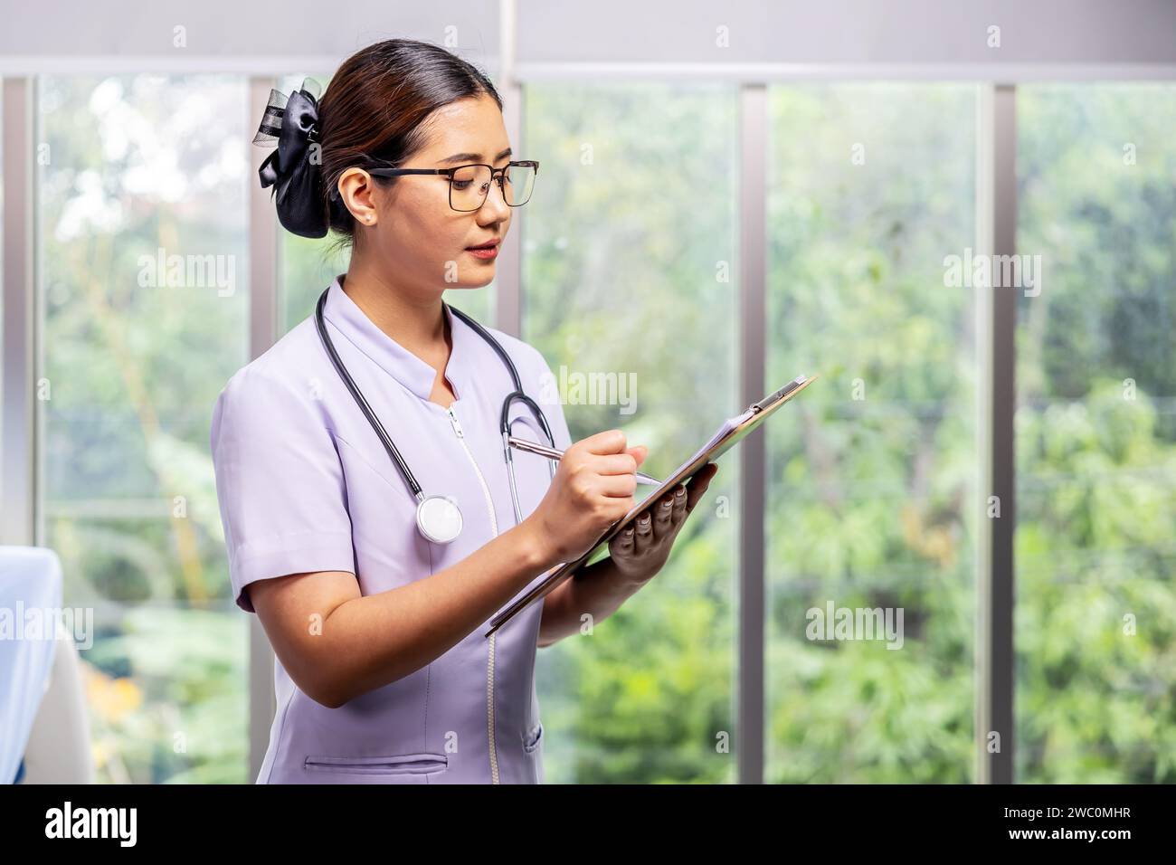 An Asian female nurse in a white lab coat holds a clipboard in a hospital Stock Photo