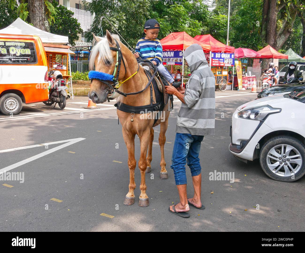 young boy preparing to ride a horse while a man holds the horse, in Bandung, West Java, Indonesia. Stock Photo