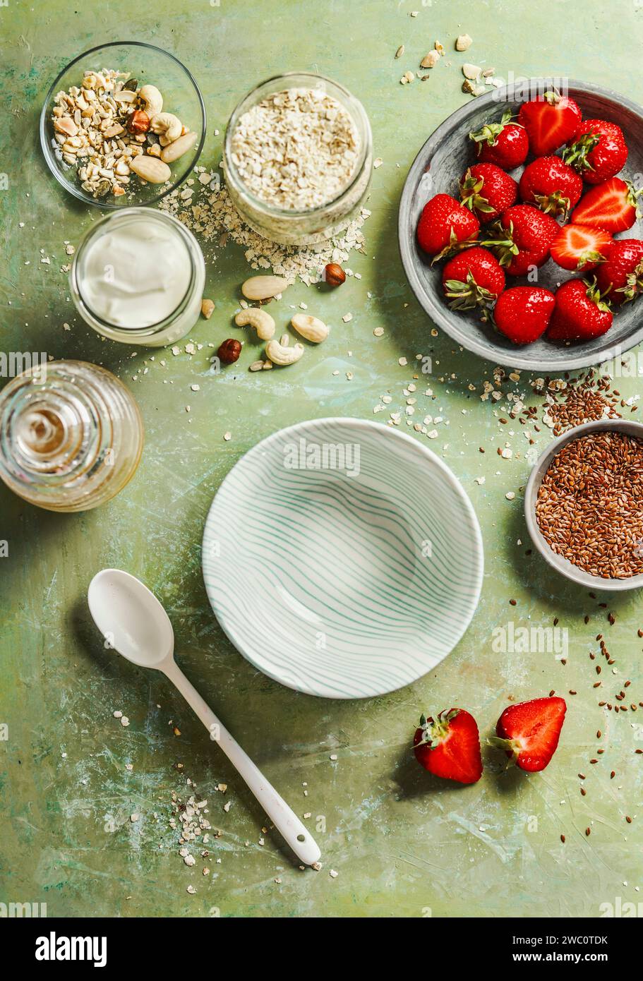 Healthy breakfast bowl preparation with oatmeal, yogurt, flax seeds,nuts and strawberries on green table background , top view Stock Photo