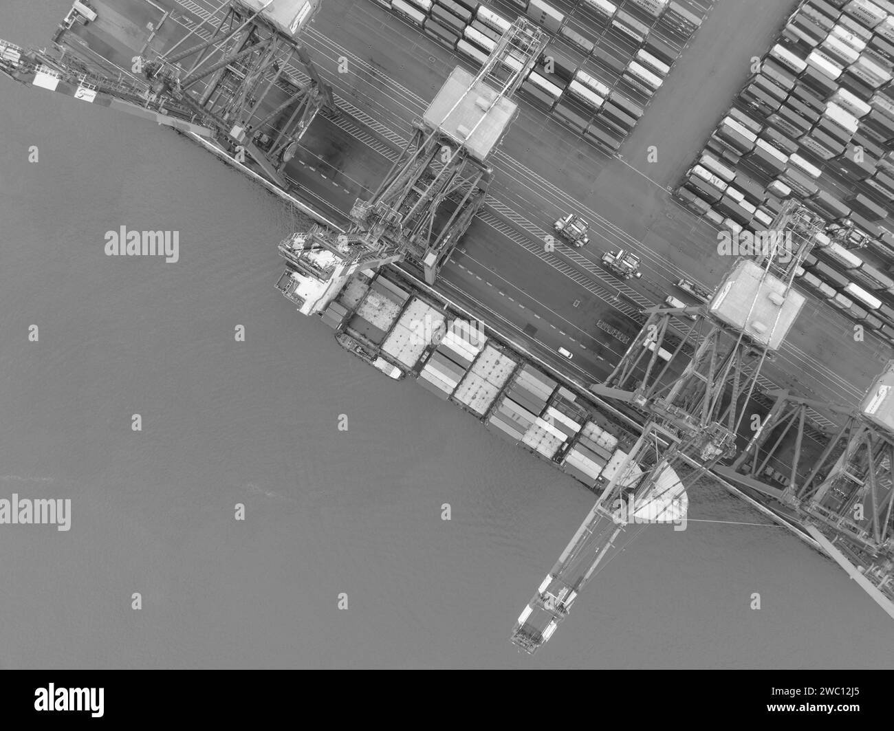 Black and white, birds eye aerial drone view on a container ship at the loading crane docks. Transportation over sea in bulk. Container shipping Stock Photo