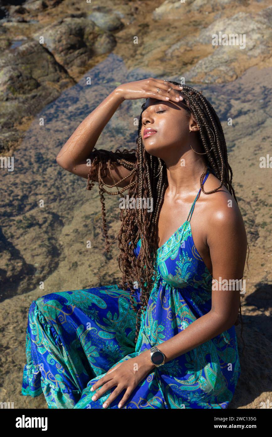 Beautiful woman in a blue dress sitting on the rocks with closed eyes ...