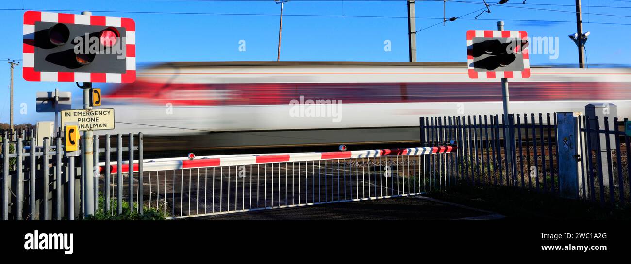 An Azuma train passing red lights at an unmanned Level crossing, East Coast Main Line Railway, Holme, Cambridgeshire, England, UK Stock Photo