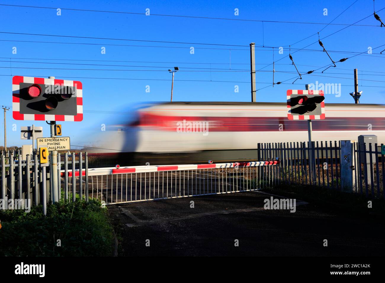 An Azuma train passing red lights at an unmanned Level crossing, East Coast Main Line Railway, Holme, Cambridgeshire, England, UK Stock Photo