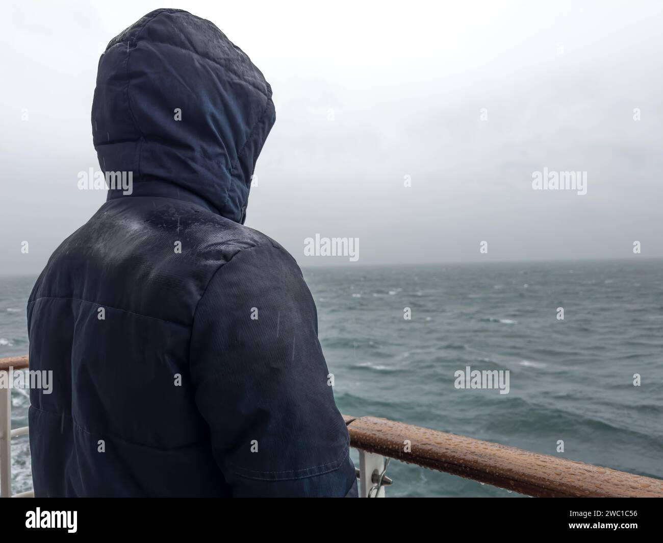 9 December 2023: Man stands with jacket on the railing of a cruise ship and looks out to sea in the rain *** Mann steht mit Jacke an der Rehling von einem Kreuzfahrtschiff und schaut bei Regen auf das Meer hinaus Stock Photo