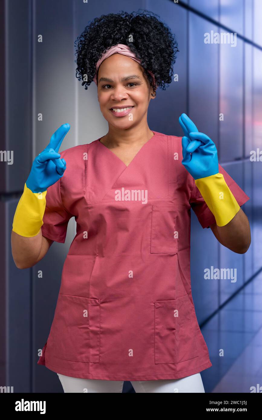 Smiling female cleaner in work clothes and rubber gloves makes a