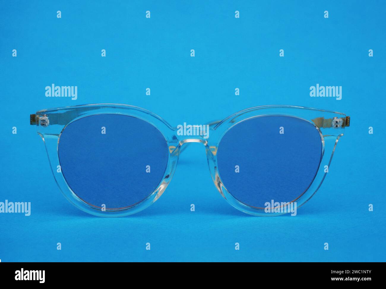 Sunglasses with a transparent frame and blue lenses on a blue paper background. Plastic glasses front view. Stock Photo