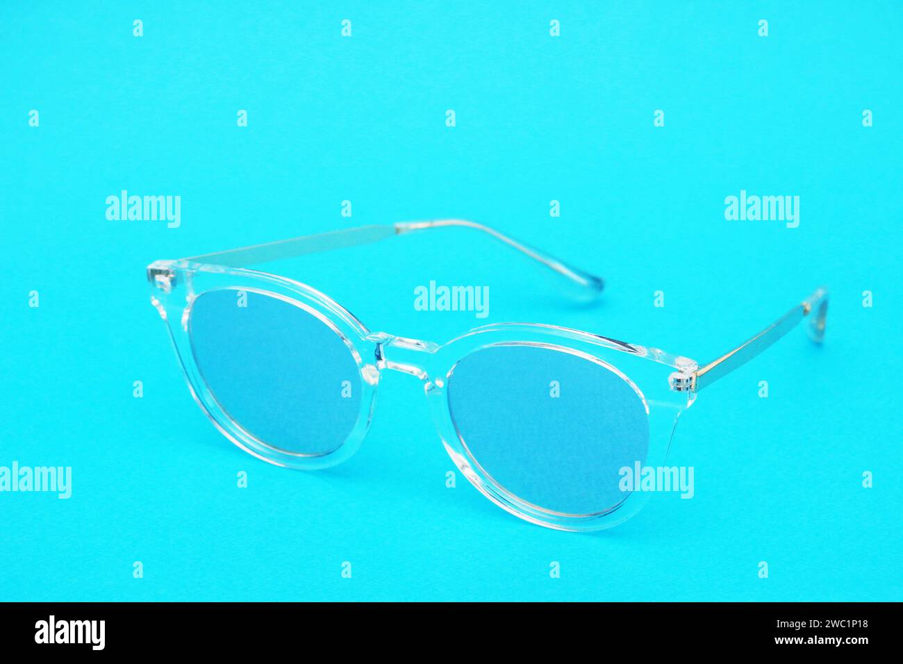 Toned image of glasses. Sunglasses with a transparent frame and blue lenses on a blue paper background. Stock Photo