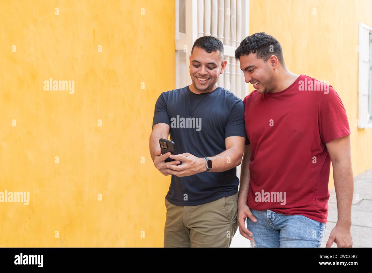 Two men share a laugh while looking at a smartphone together. Stock Photo
