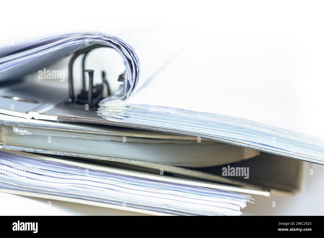 Part of an open ring binder with many documents on a stack of more file folders, business and office concept fading to a white background, copy space, Stock Photo