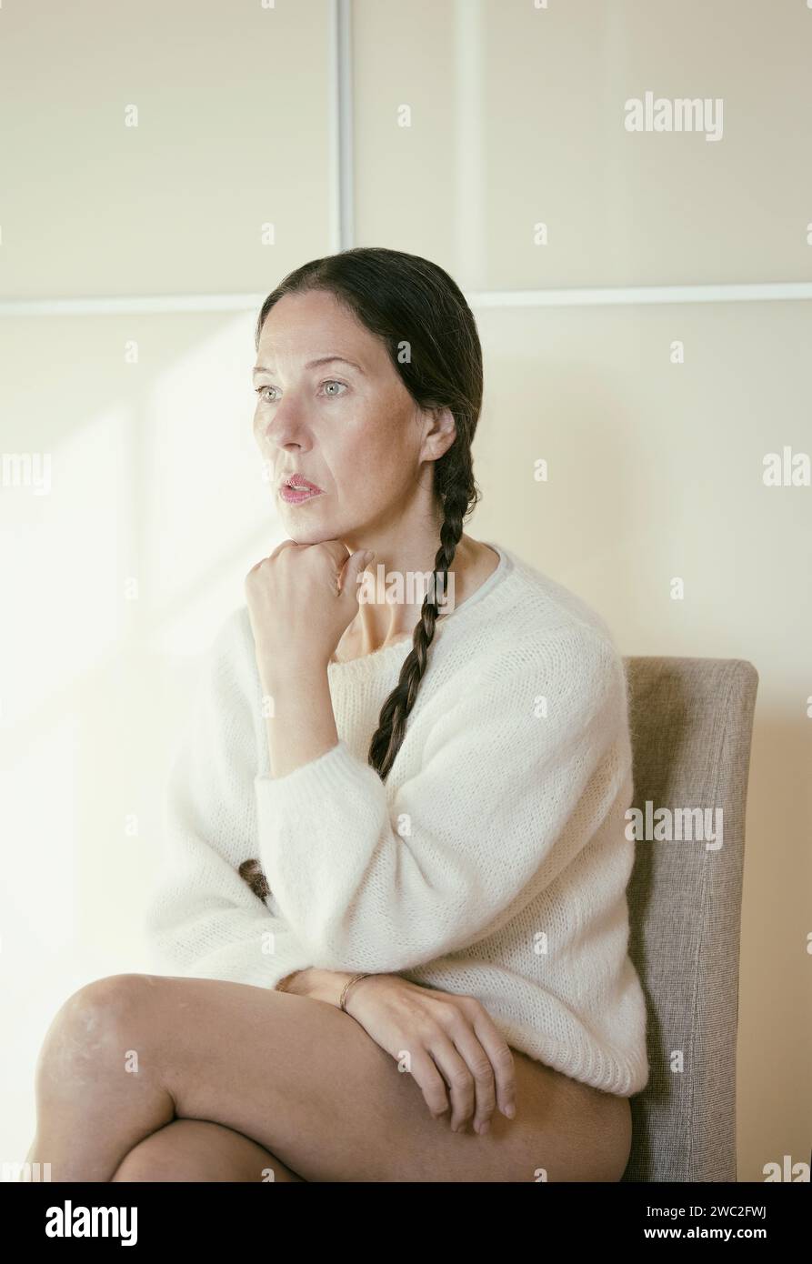 woman sitting on a chair with white wool sweater in thoughtful attitude, france Stock Photo