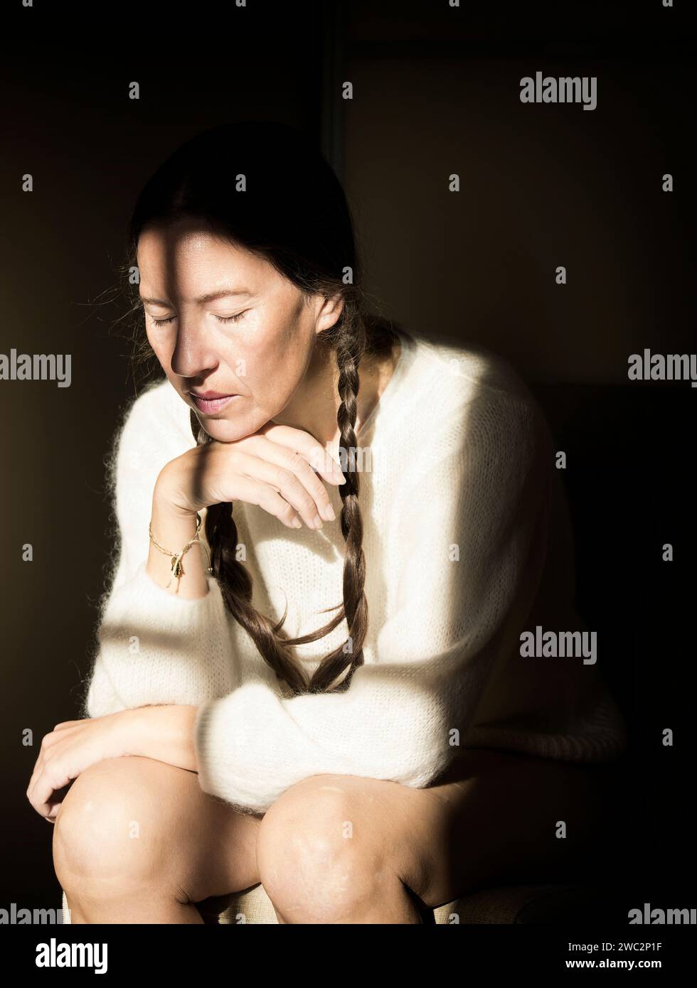 woman sitting on a chair with white wool sweater in thoughtful attitude II, france Stock Photo