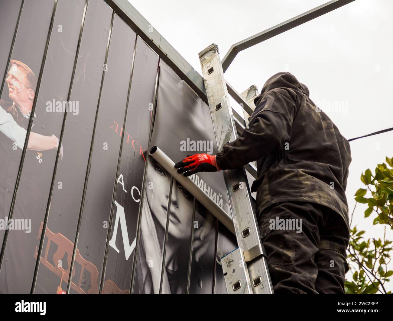 Sochi, Russia - February 2023, 23: A worker unrolls a roll of an outdoor advertising banner for billboard sticker Stock Photo