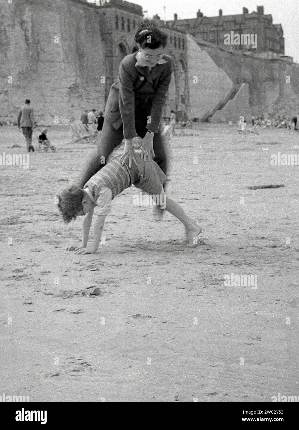 1960s, historical, a mother having fun with her son, playing a game of leapfrog on the beach at Margate, Kent, England, UK. Stock Photo