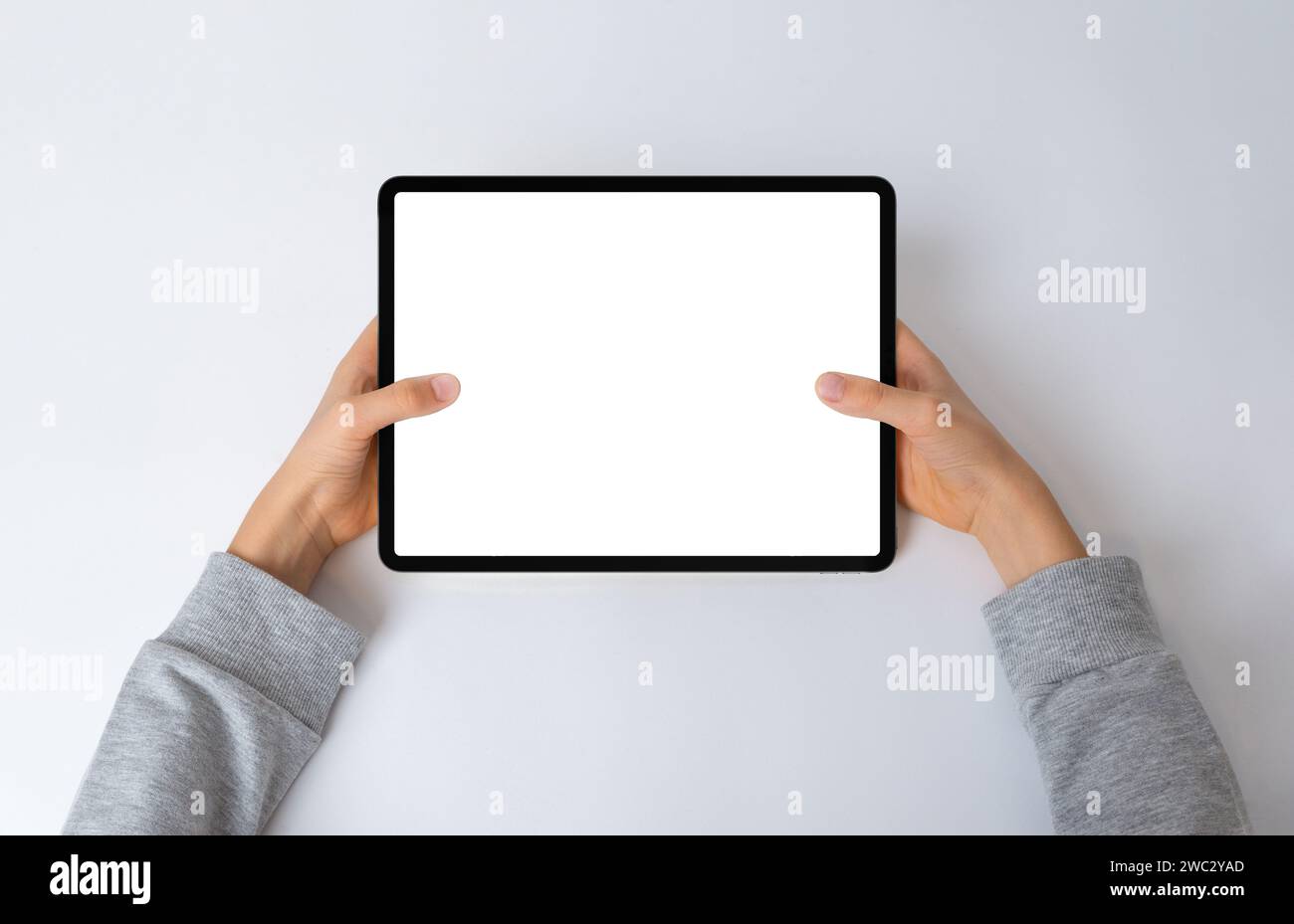 Top view of a kid's hands holding a horizontal tablet on a desk. Flat lay composition with an isolated screen for mockup, perfect for showcasing inter Stock Photo