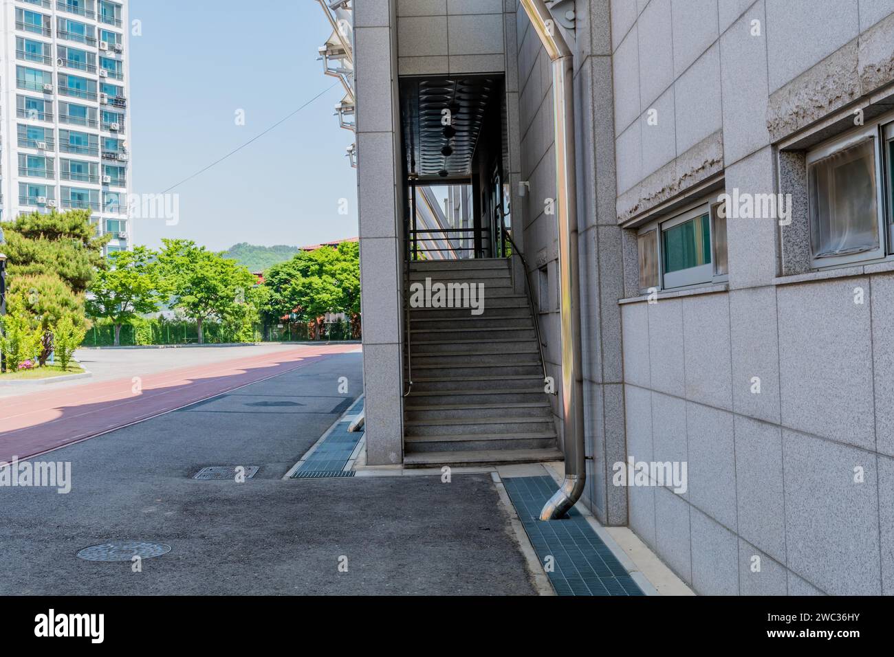 Rear entrance stairway into sports stadium with vacant paved lot, trees and blue sky in background Stock Photo