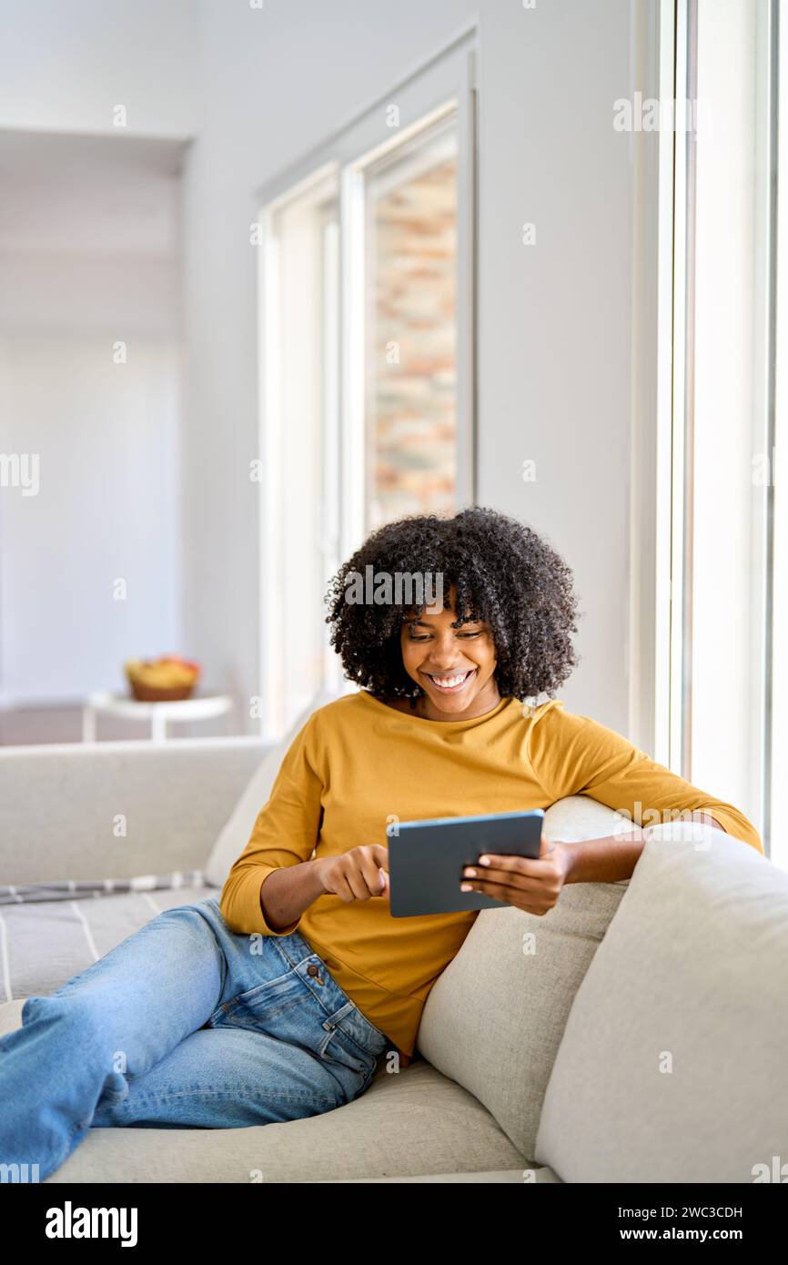 Happy young African American woman using digital tablet on couch at home. Stock Photo