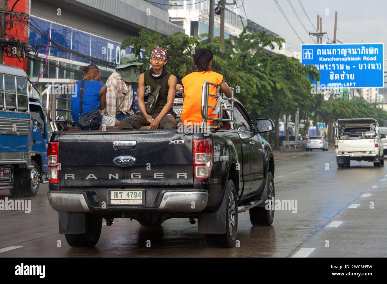 SAMUT PRAKAN, THAILAND, OCT 11 2023, Young men sit in the back of a pickup truck while driving through the city Stock Photo