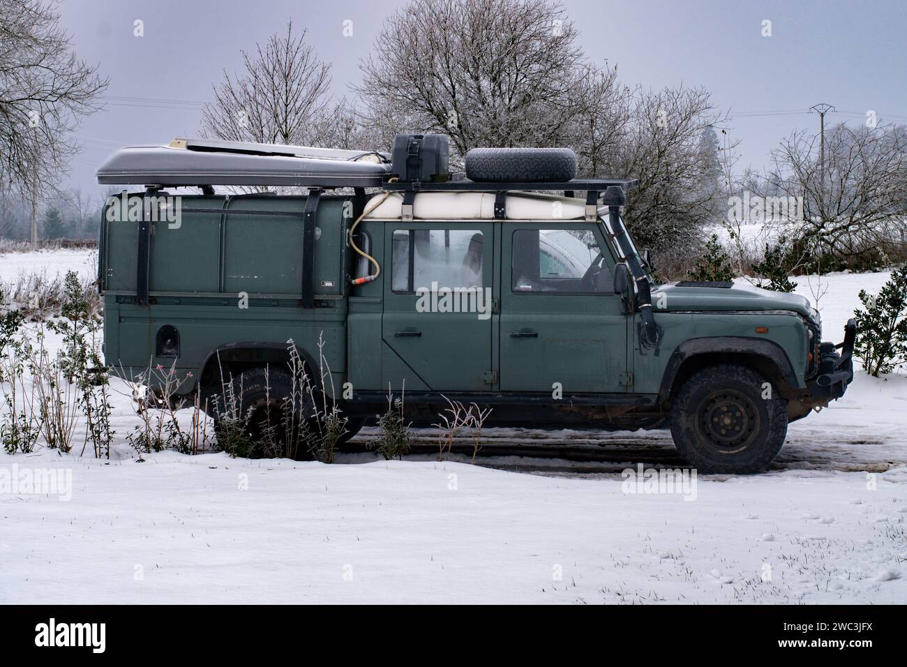 Vintage land rover defender in snow covered background. Vintage Land Rover Defender SUV parked in a serene winter landscape covered in fresh snow. The Stock Photo