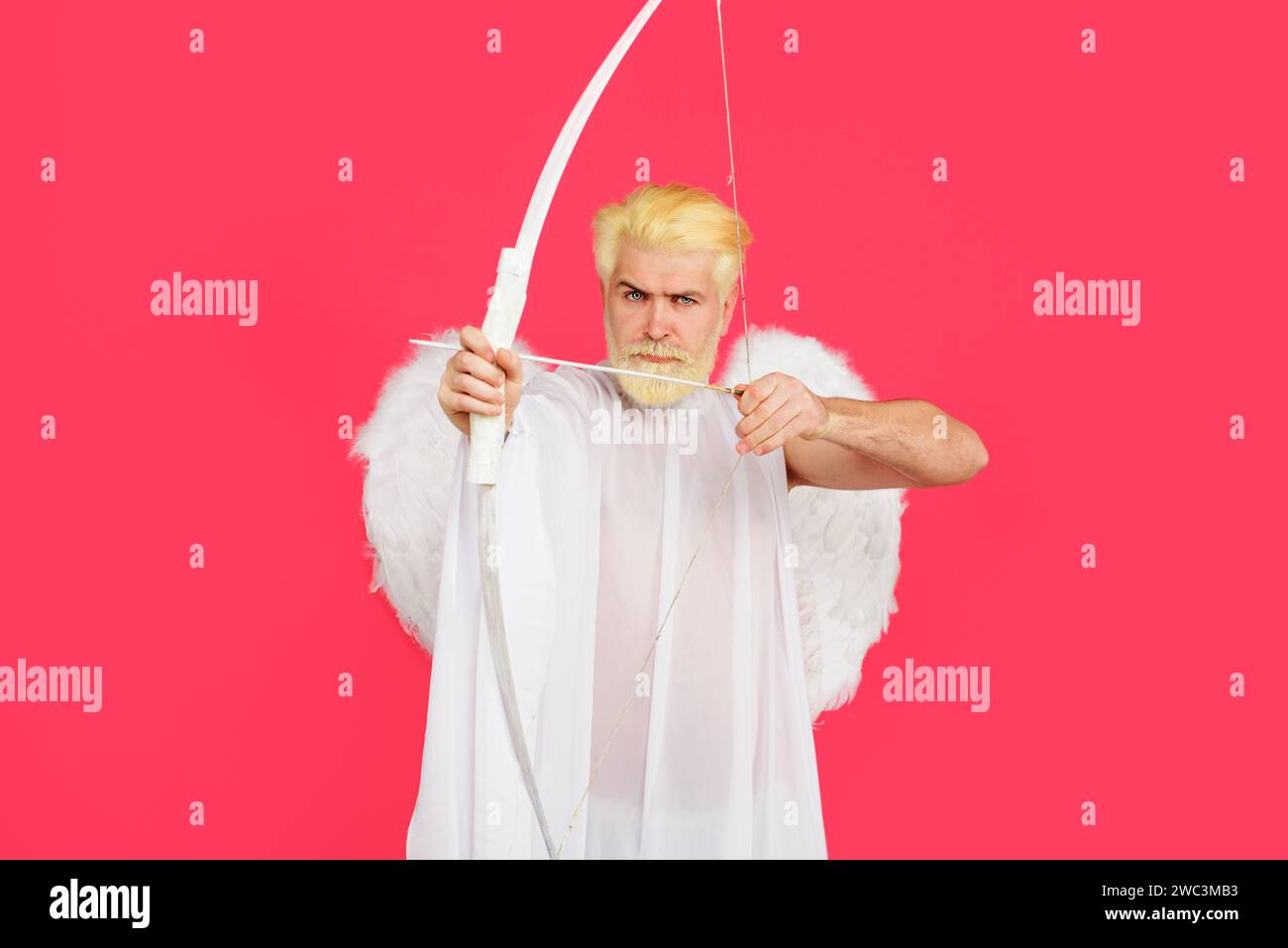 Valentines day celebration. Male cupid in angel wings shoots at target with arrow. God of love. Valentine cupid angel shooting arrows of love. Serious Stock Photo