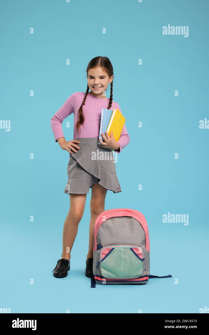 Cute schoolgirl with books on light blue background Stock Photo - Alamy