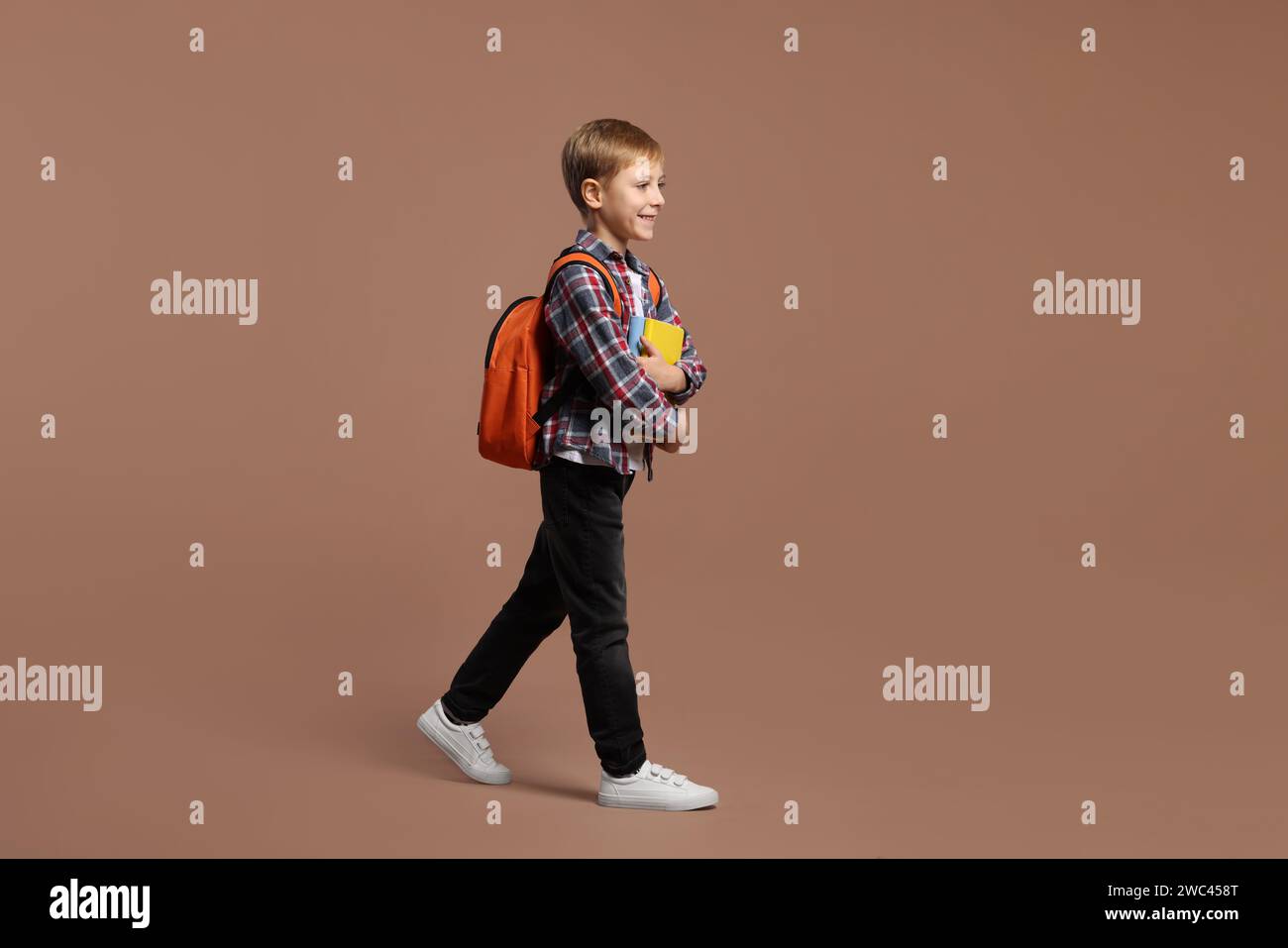 Happy schoolboy with backpack and books on brown background Stock Photo ...