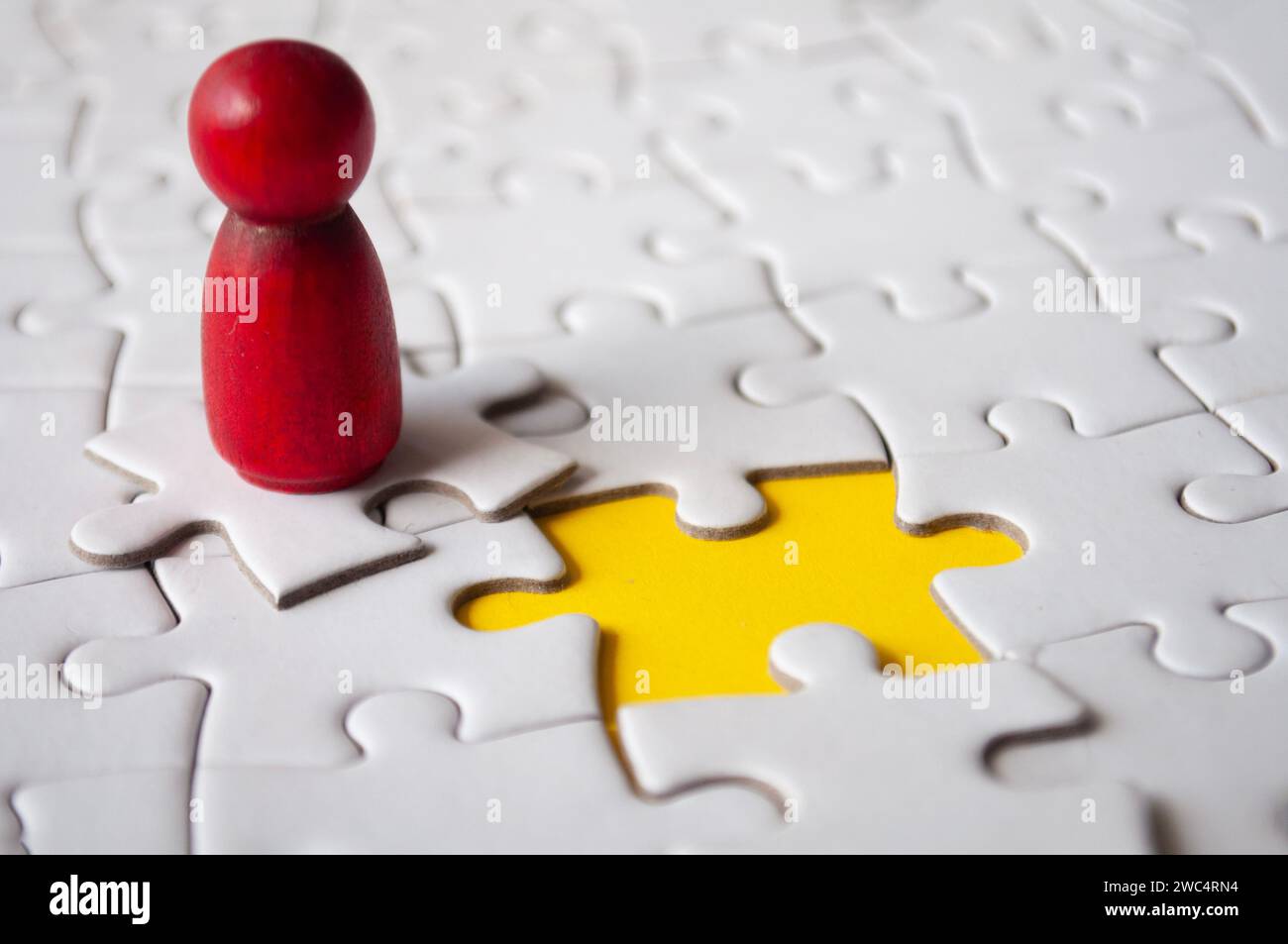 Red wooden doll on top of jigsaw with missing jigsaw puzzle. Hiring and employment concept. Stock Photo