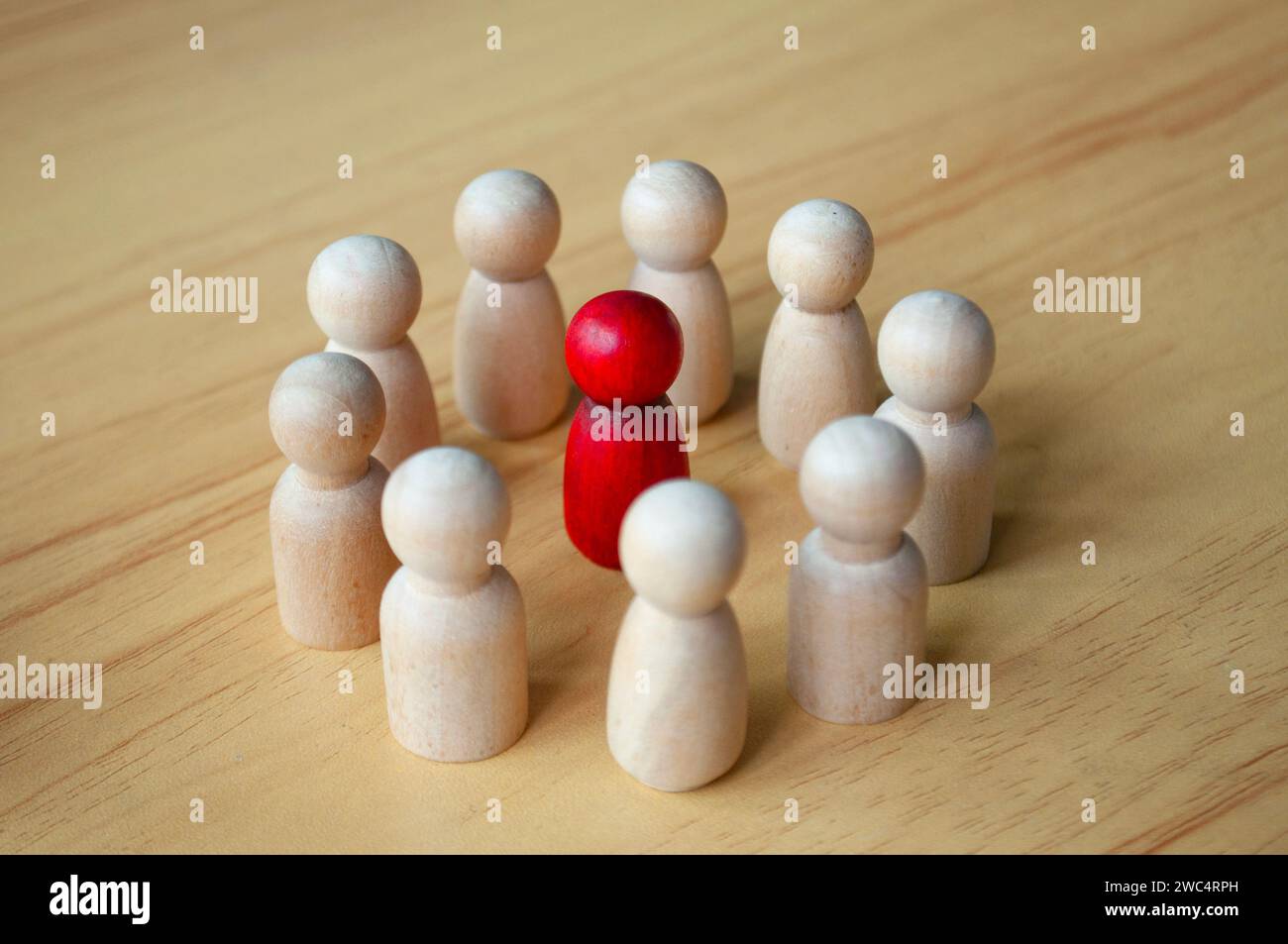 Close up of red wooden doll surrounded by other dolls. Representing either leadership or harassment. Stock Photo