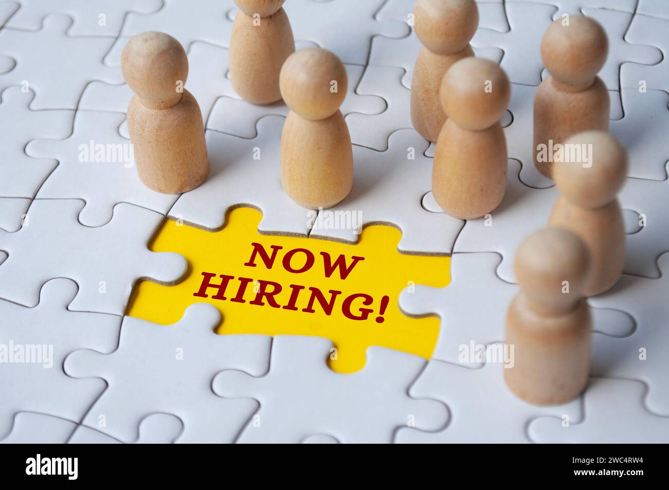 Now hiring text on missing jigsaw puzzle with wooden dolls.. Hiring and employment concept Stock