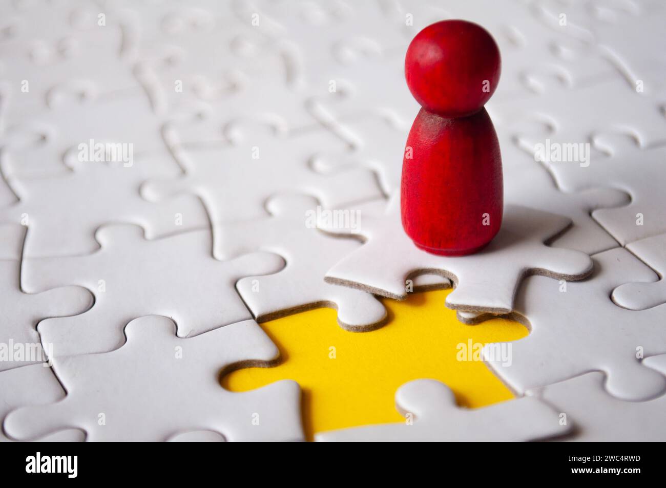 Red wooden doll on top of jigsaw with missing jigsaw puzzle. Hiring and employment concept. Stock Photo
