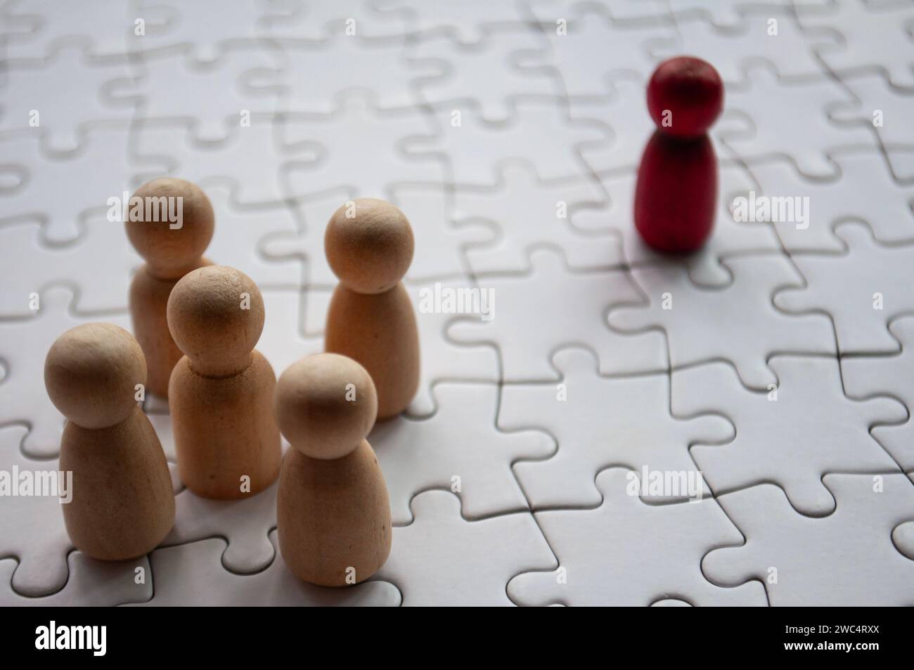 Red wooden doll leading on top of jigsaw puzzle. Stock Photo