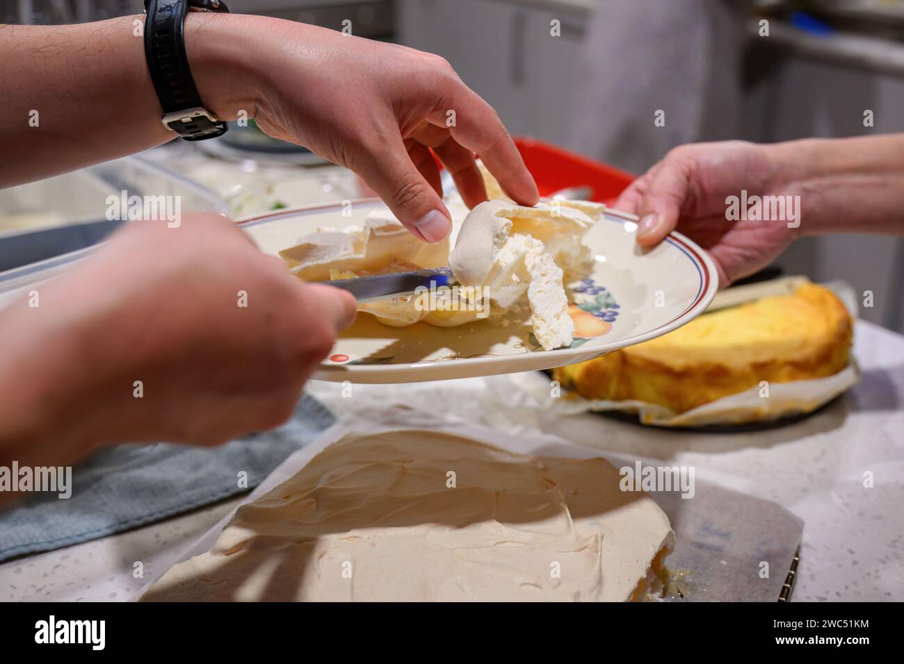 Hands holding a plate and sharing pavlova over the kitchen benchtop. Home cooking and entertainment concept. Stock Photo