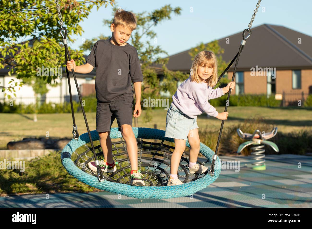 Brother and sister are playing on the playground outside. Children ride ...