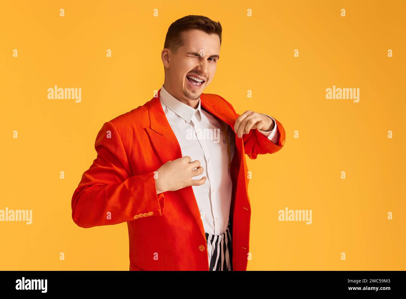 stylish winking young man in orange jacket and striped pants on vibrant ...