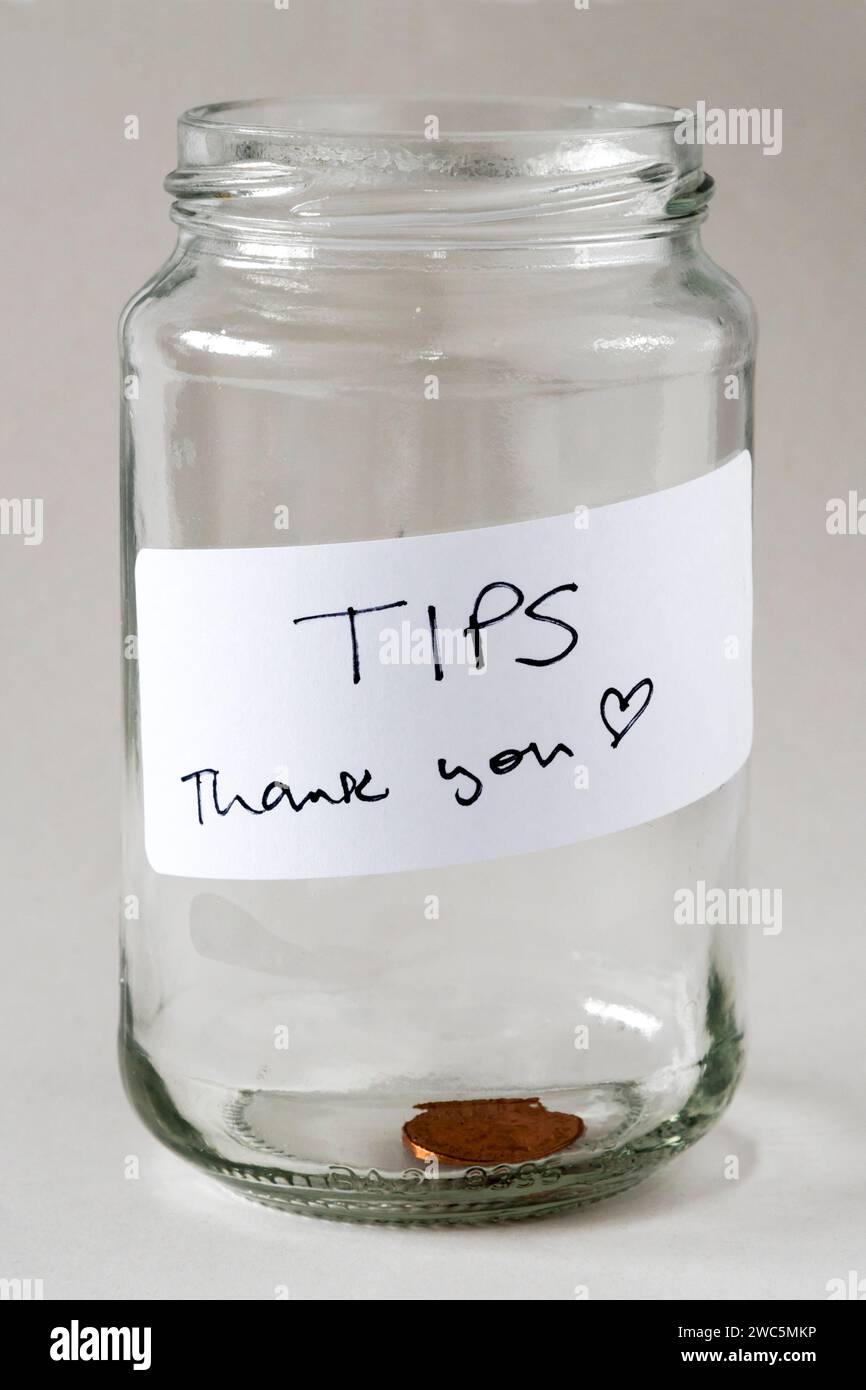 A tips jar with a label reading Tips Thank you and only a single penny in the bottom. Stock Photo