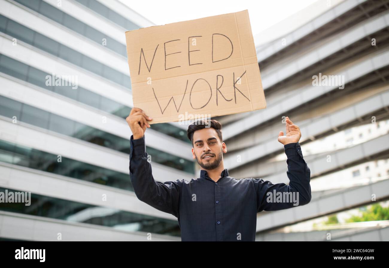 arab man stands against urban backdrop holding NEED WORK sign Stock ...