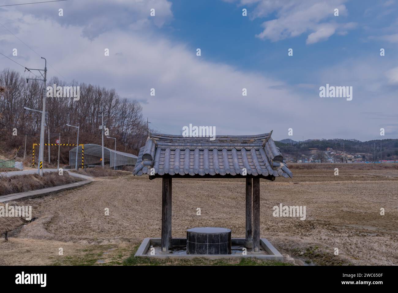 Covered water well under ceramic tiled roof full of water in a mountainside public park with plowed field in background Stock Photo