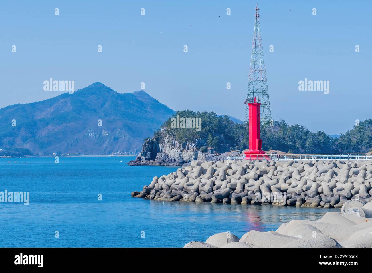 Red lighthouse on concrete pier in small coastal fishing port Stock Photo