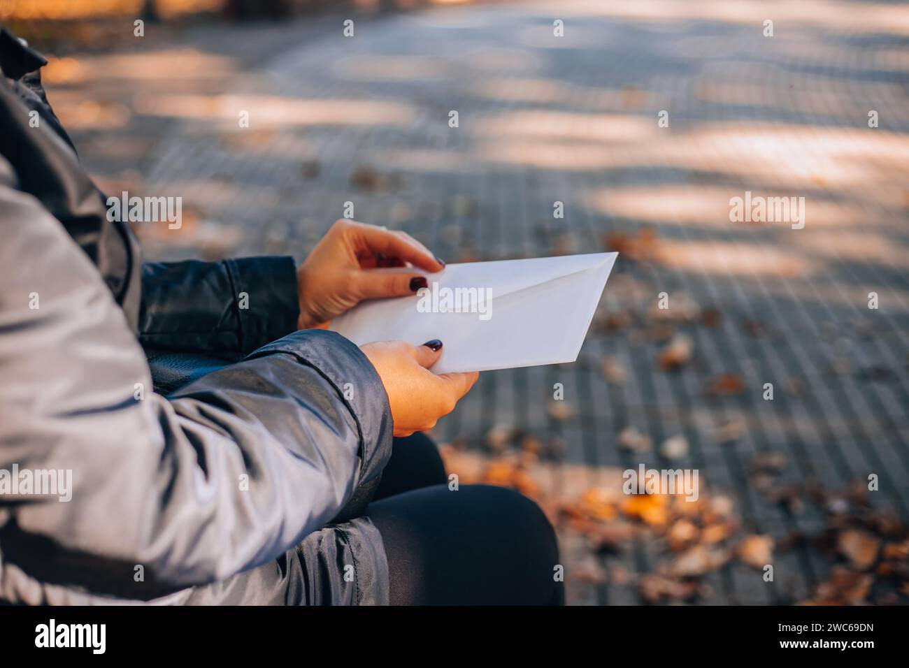 Woman opens a white envelope with a letter. Autumn foliage in the background. Stock Photo