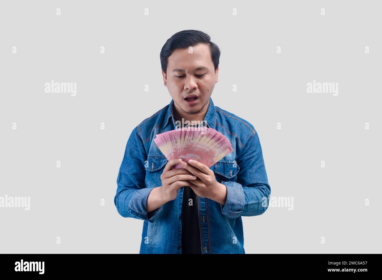Young Asian man showing stunned face expression while holding paper money Stock Photo
