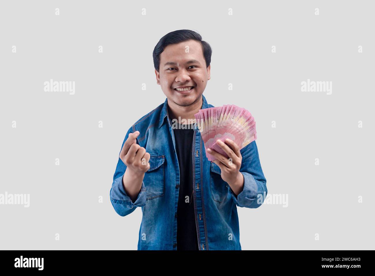 Young Asian man showing smilling face expression while holding paper money and love sign hand Stock Photo