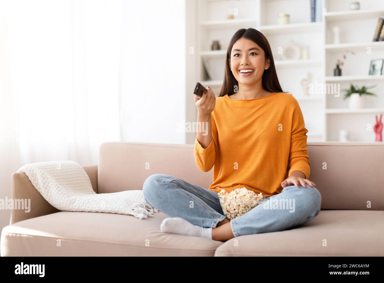 Happy young chinese lady enjoying time at home, watching TV Stock Photo