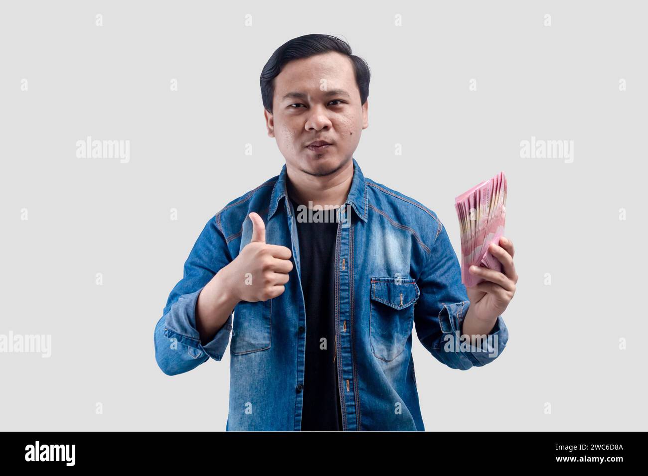 Young Asian man showing proud face expression while holding paper money and give a thumbs up Stock Photo