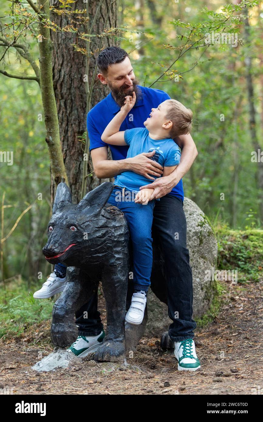 Portrait of a son and father on a wolf sculpture against a background of green nature. Stock Photo